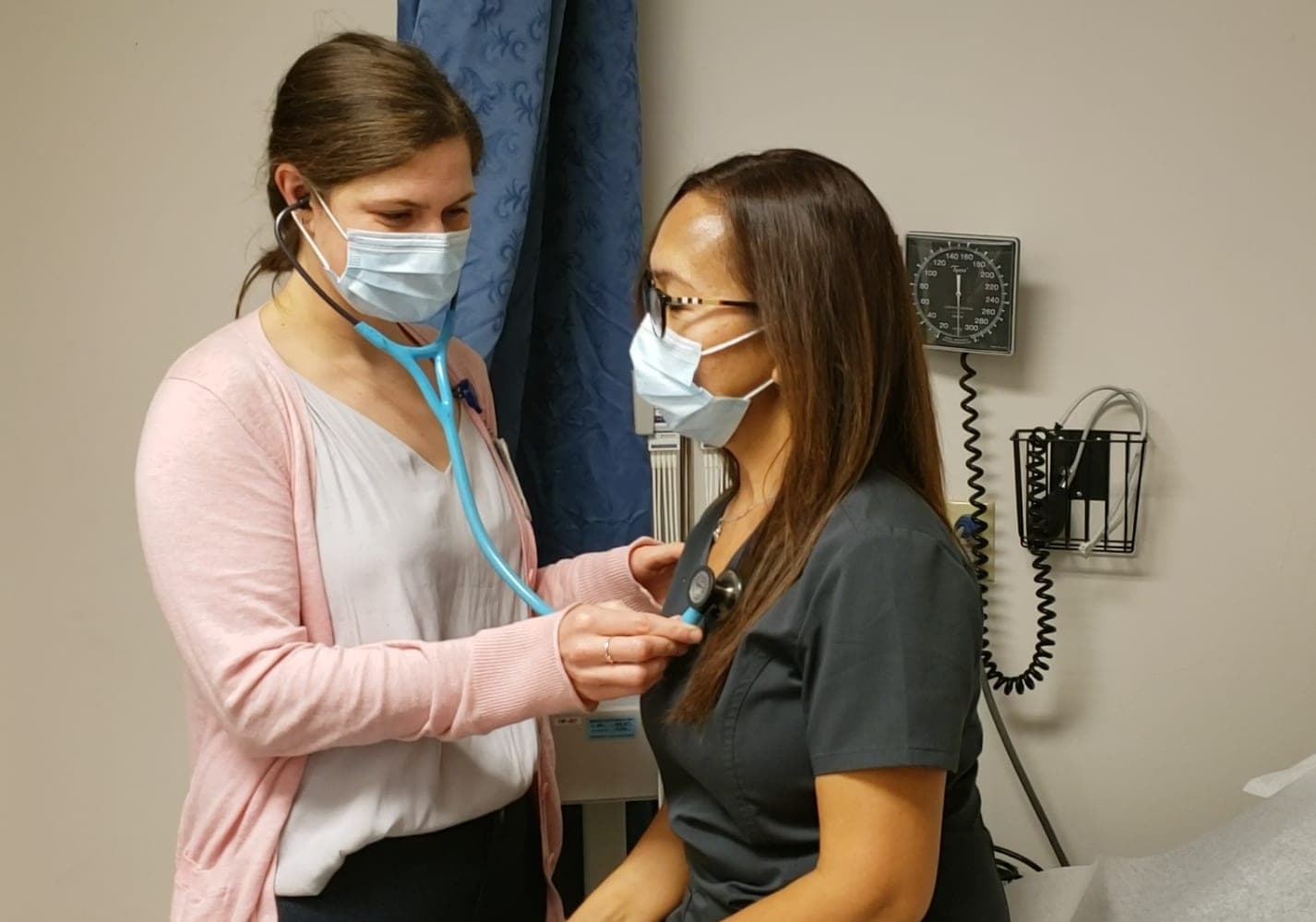 A resident listening to a patient's heart with a stethoscope in a clinic exam room