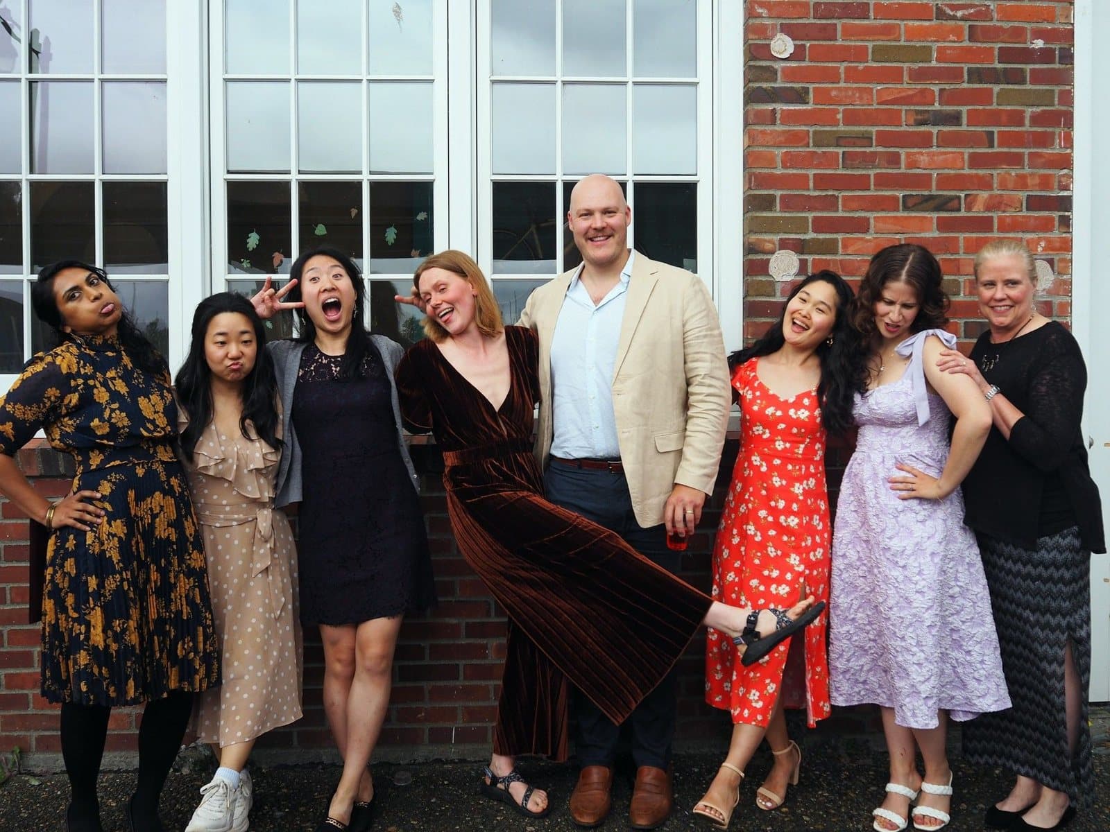 The class of 2025 striking playful poses in front of a brick wall and tall white windows