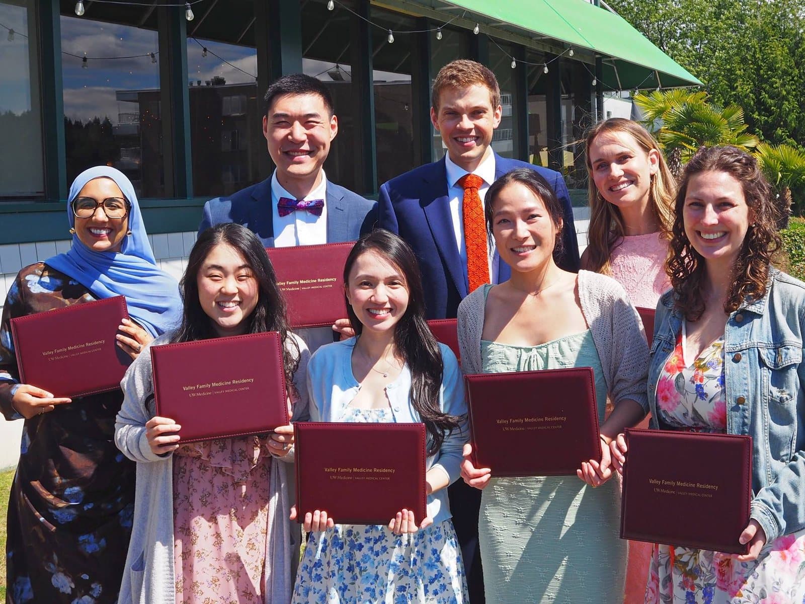 The class of 2026 smiling outdoors, each holding a maroon Valley Family Medicine Residency diploma folder