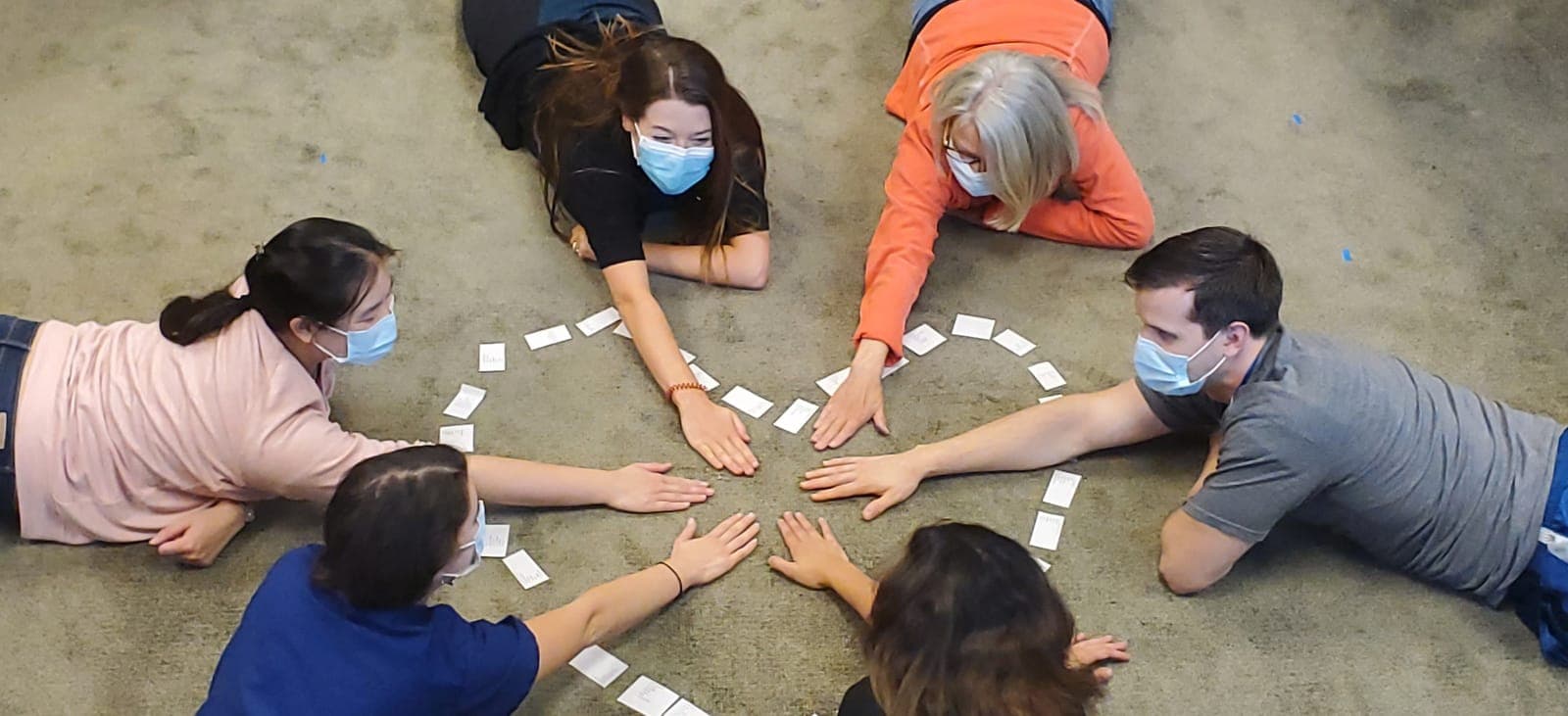 Residents lying on the floor in a circle, their hands meeting in the middle of a heart outline