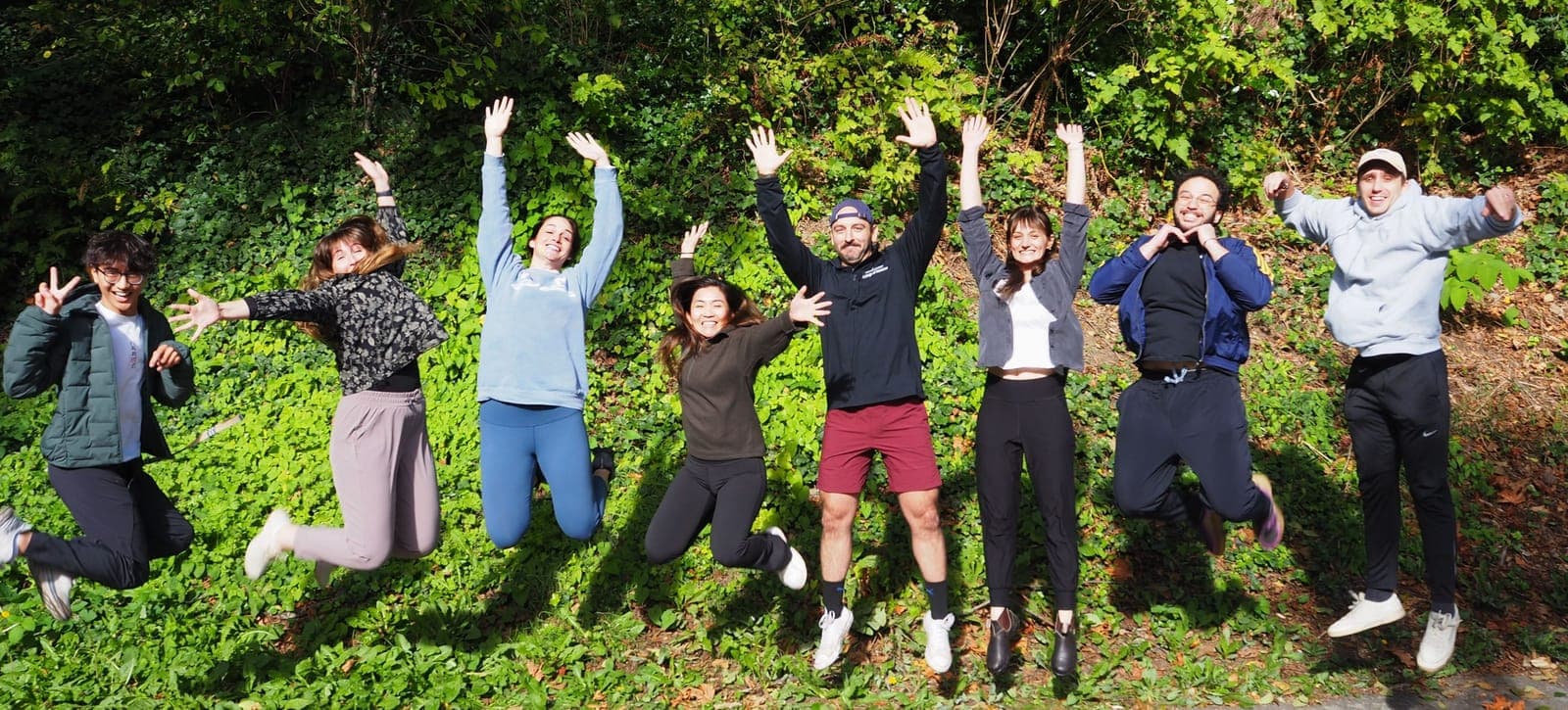 Residents jumping in the air with arms raised on a leafy hillside