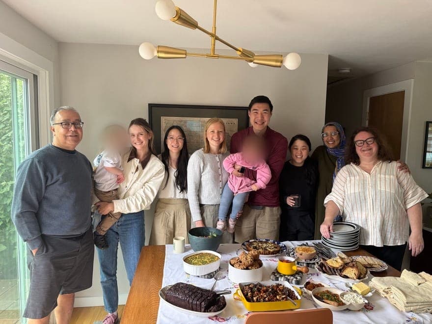 Residents, faculty and their families around a table of food at a home gathering