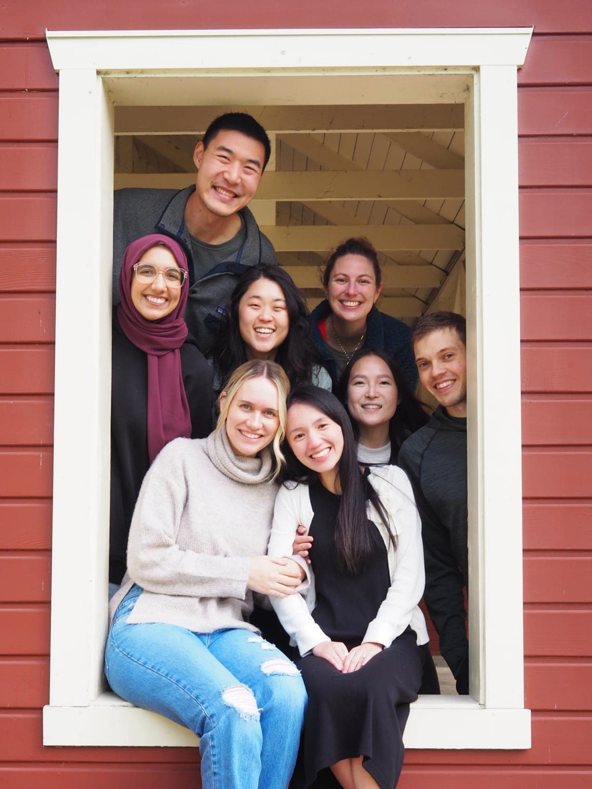 Residents from the class of 2026 posing in the window frame of a red cabin