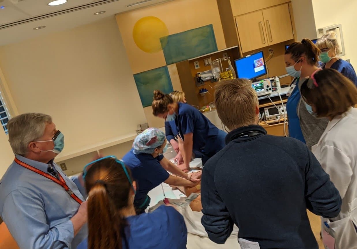 A team performing chest compressions on a simulation mannequin in a labor and delivery room while faculty and nurses look on
