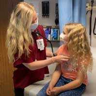 A resident listening to a young patient's heart with a stethoscope in an exam room