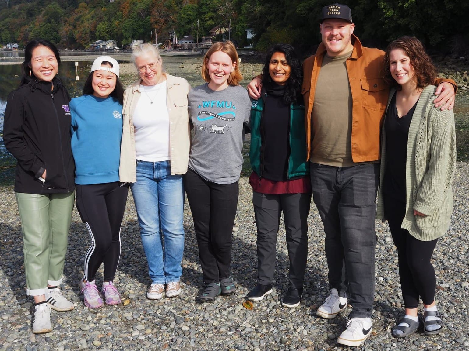 Seven residents from the class of 2025 standing arm in arm on a pebble beach on Puget Sound