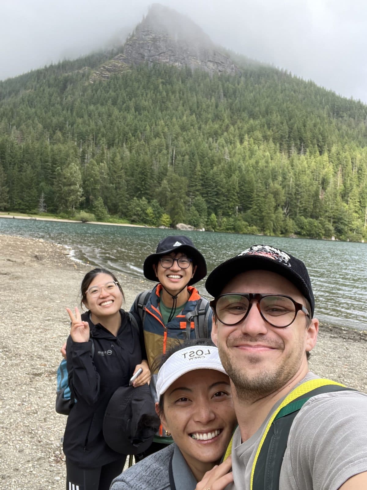 Four residents taking a selfie on the shore of a mountain lake below a forested peak