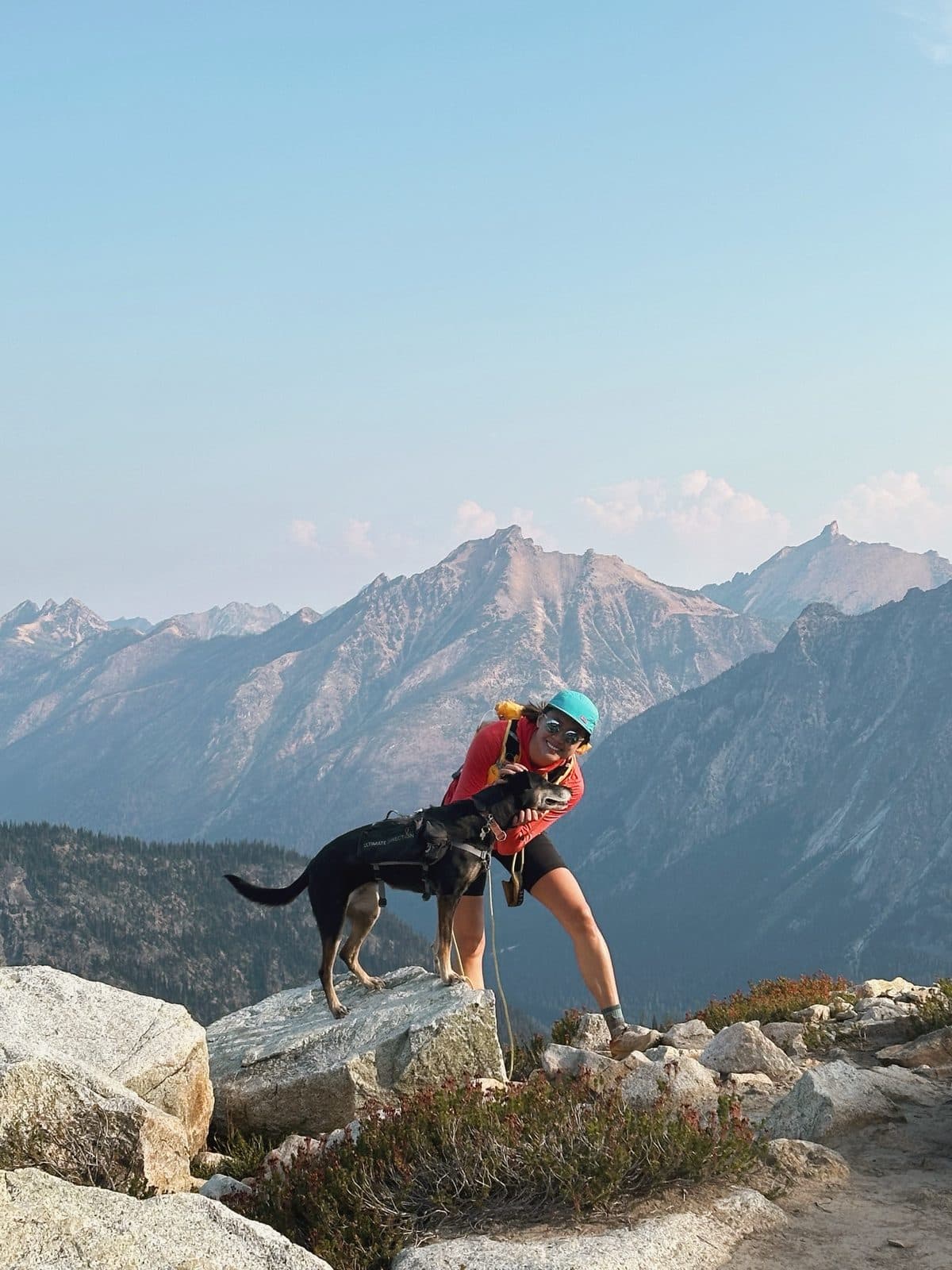Vivian Cheng and her dog on a rocky ridge above a valley of jagged peaks