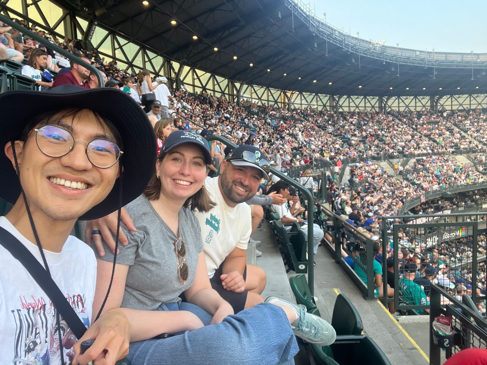 Three residents smiling in the stands at a packed Mariners baseball game