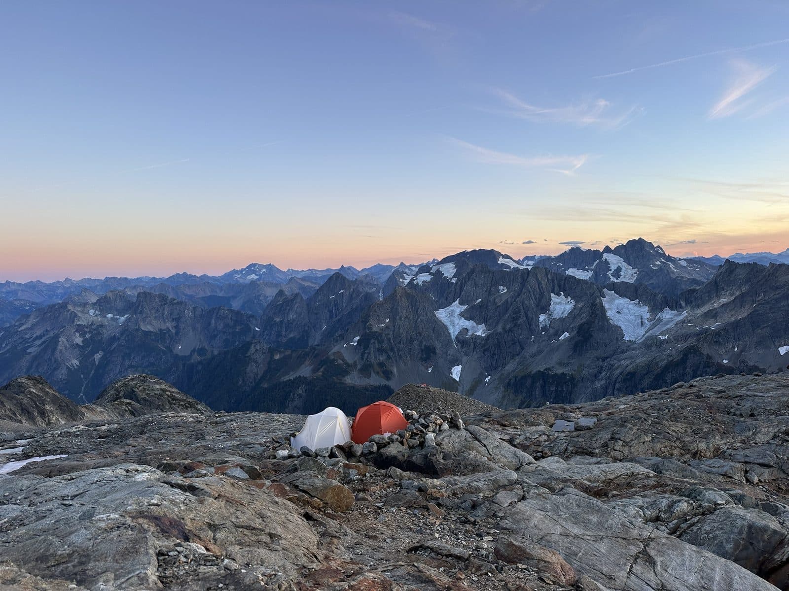 Two tents on a rocky alpine ridge at sunset, facing glaciated peaks