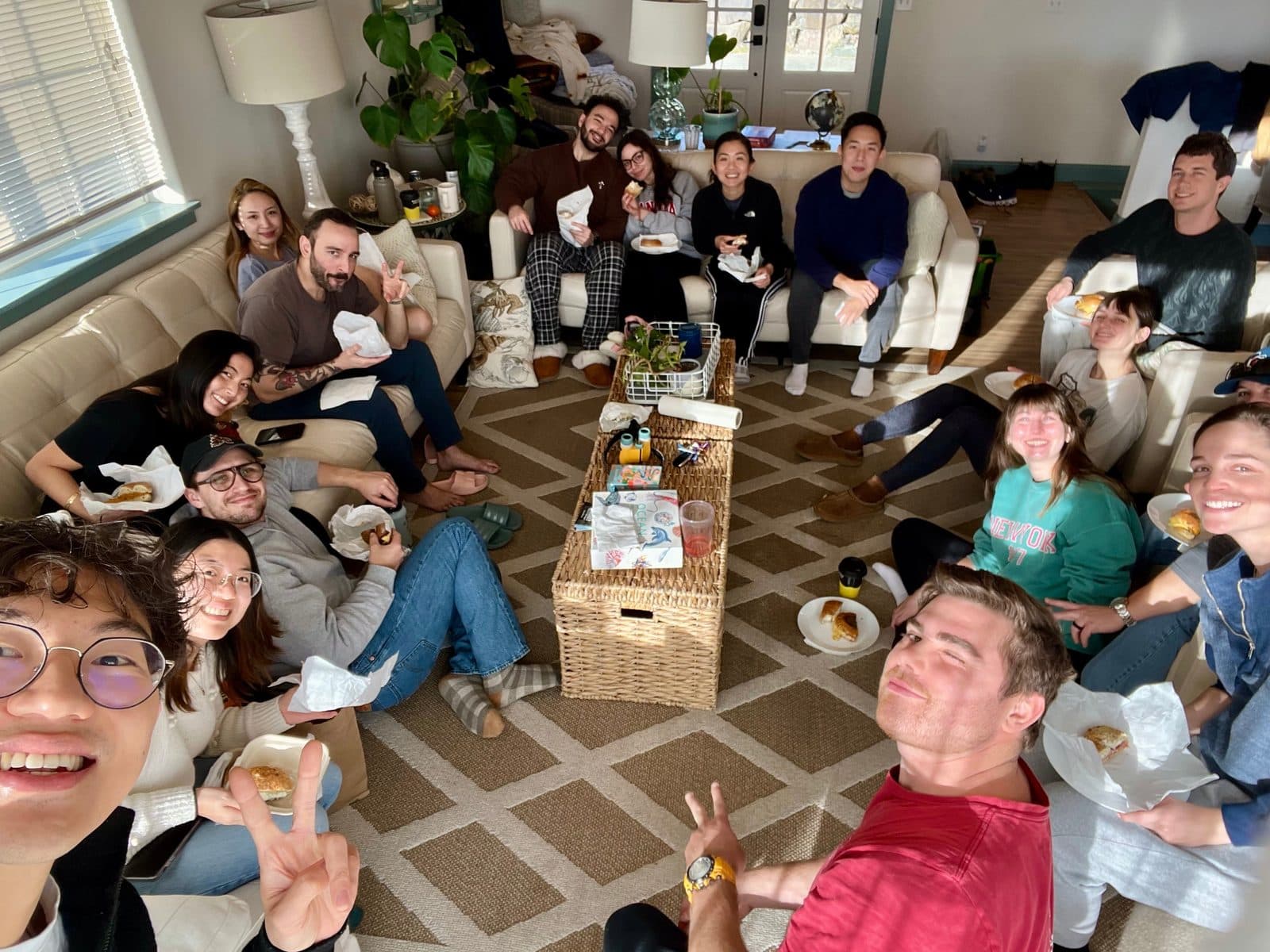 Residents from the class of 2027 relaxing on couches and the floor of a sunny cabin living room, sharing food