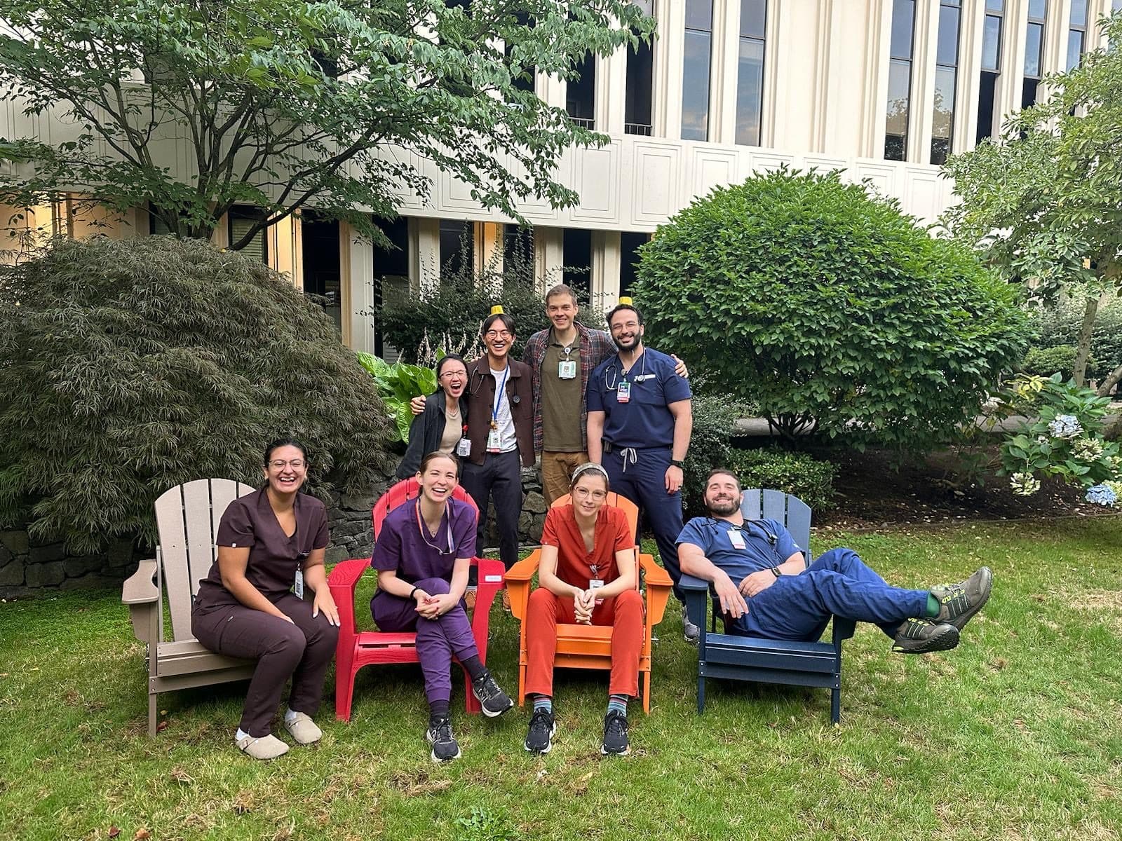 An inpatient team in scrubs sitting in colorful Adirondack chairs in the hospital's healing garden
