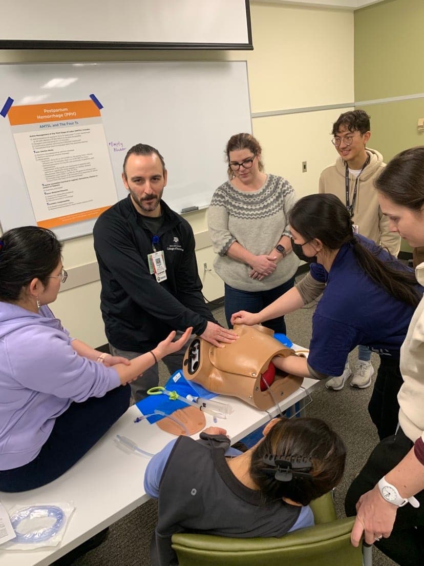 Residents and faculty gathered around an obstetric simulation model on a table