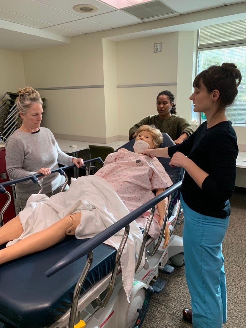 A faculty member coaching a resident at a full-body obstetric simulation mannequin on a stretcher