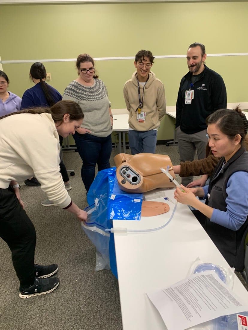 A resident working with an obstetric simulation model while classmates watch