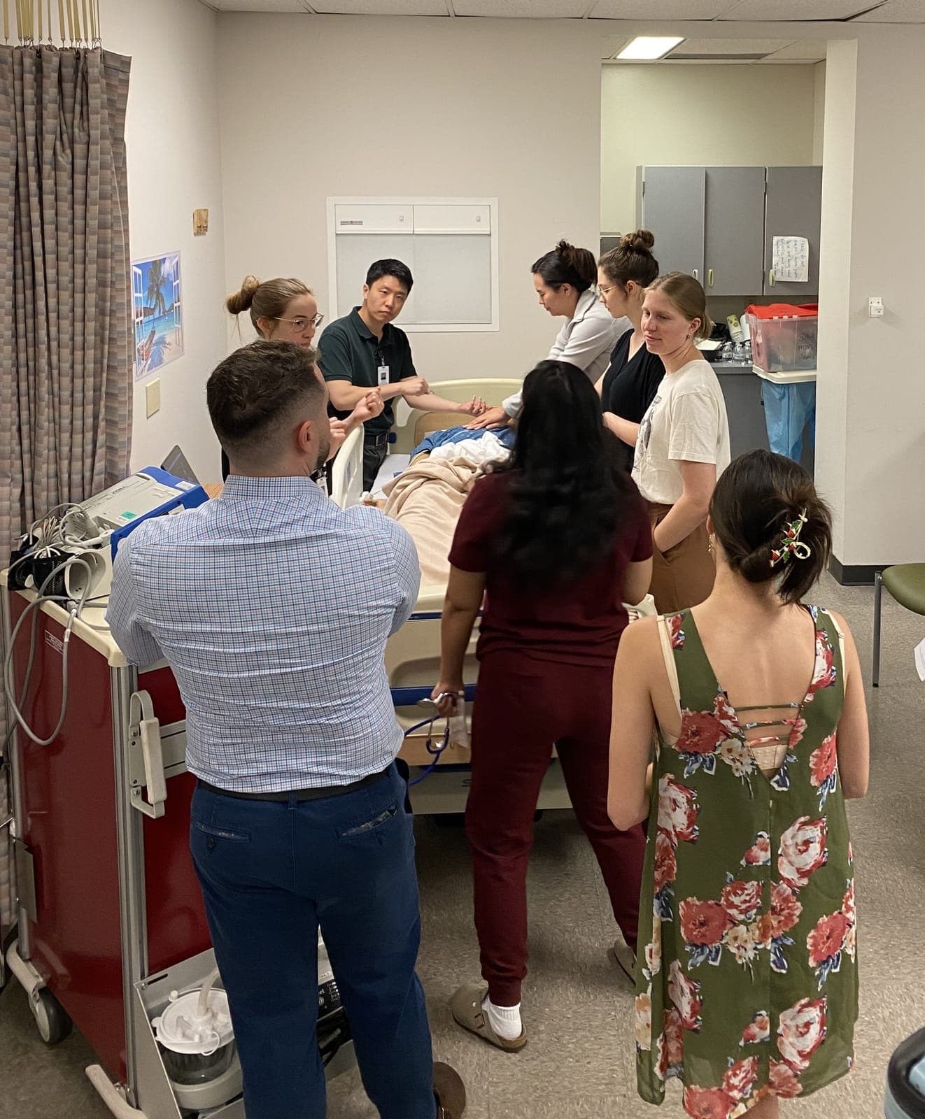 Residents around a simulation mannequin in a hospital bed during a mock code, with a crash cart nearby