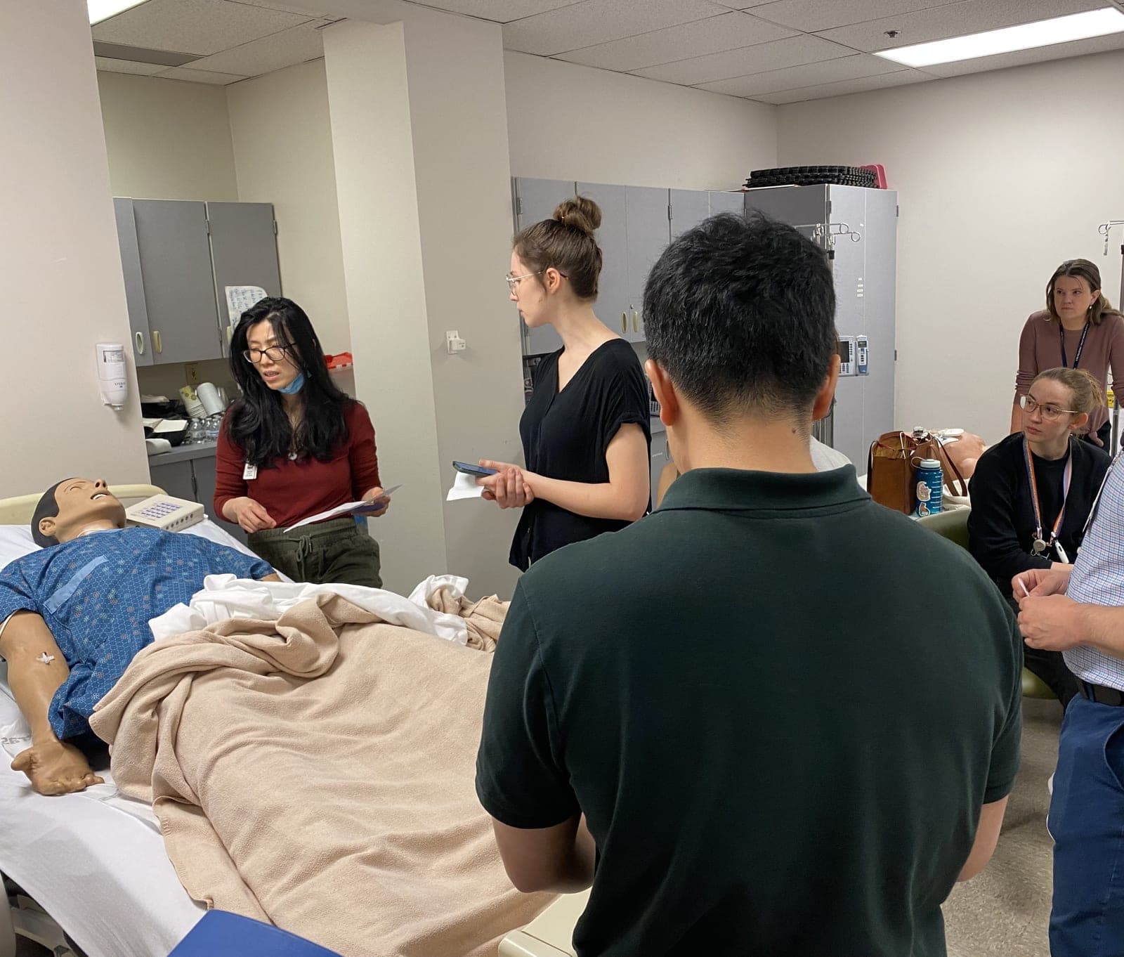 Residents and faculty gathered around a simulation mannequin in a hospital bed, one reading from a clipboard