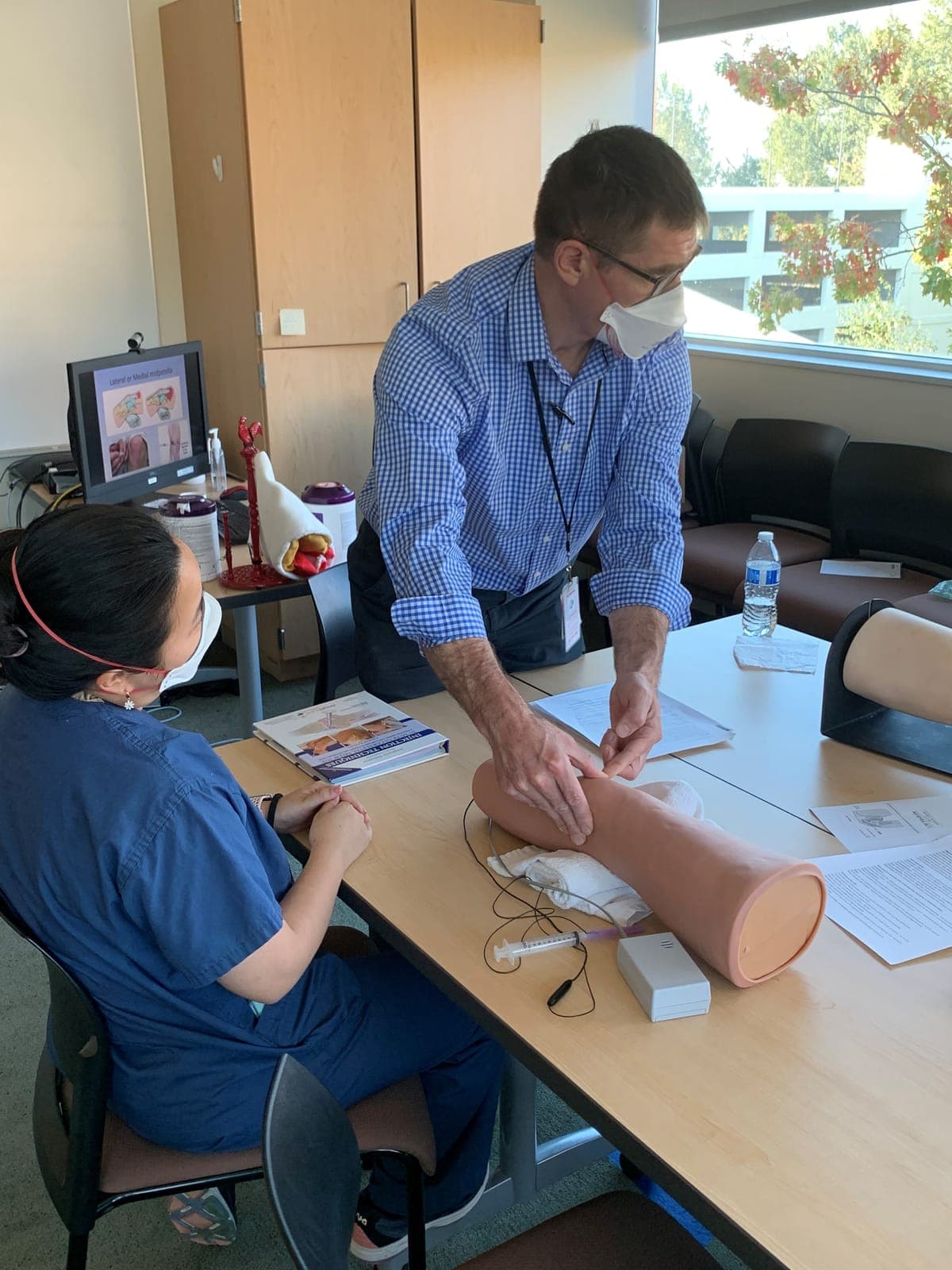 A faculty member guiding a resident through a knee injection on a leg model