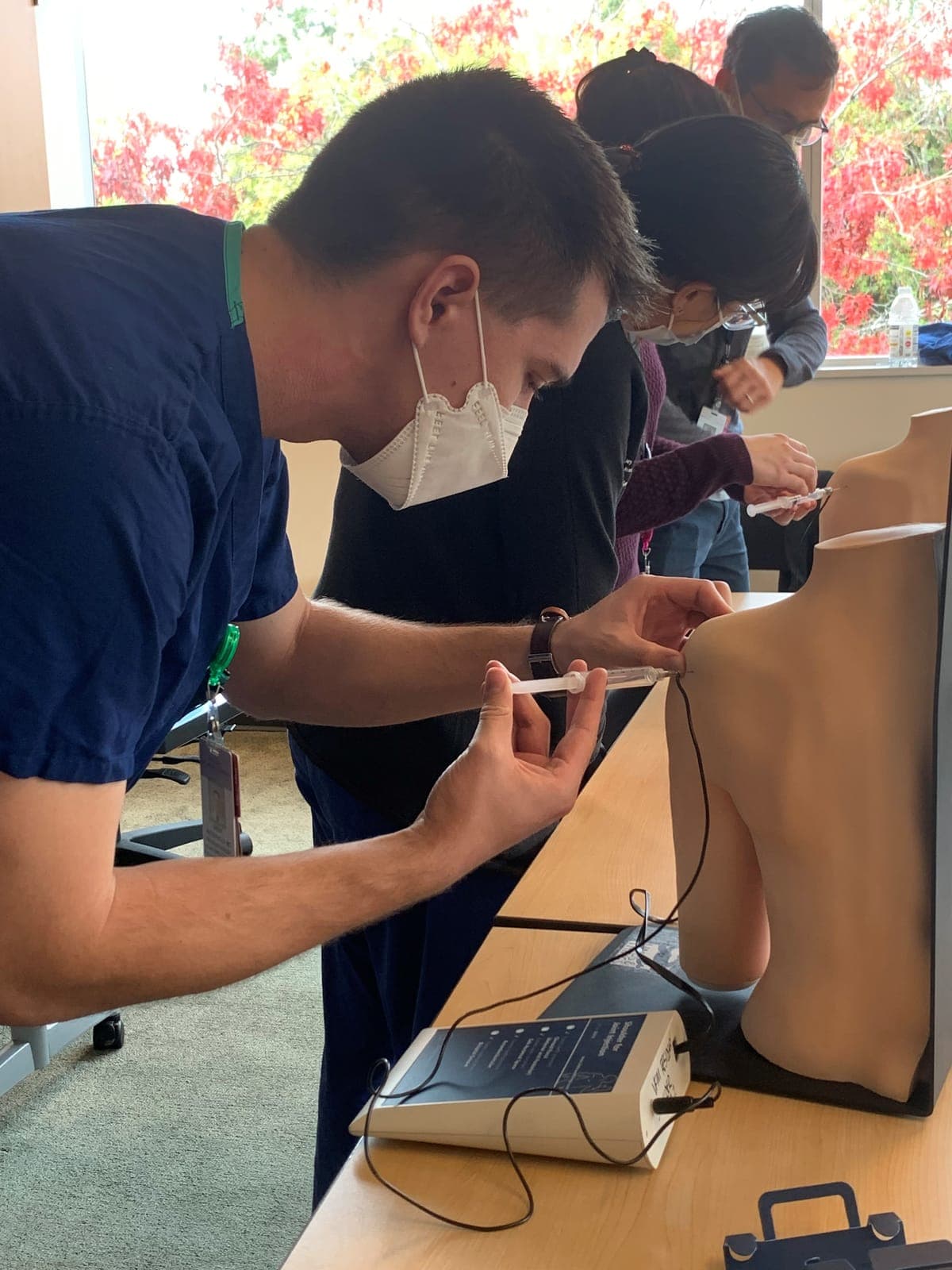 A resident practicing a shoulder injection on a torso model as others watch