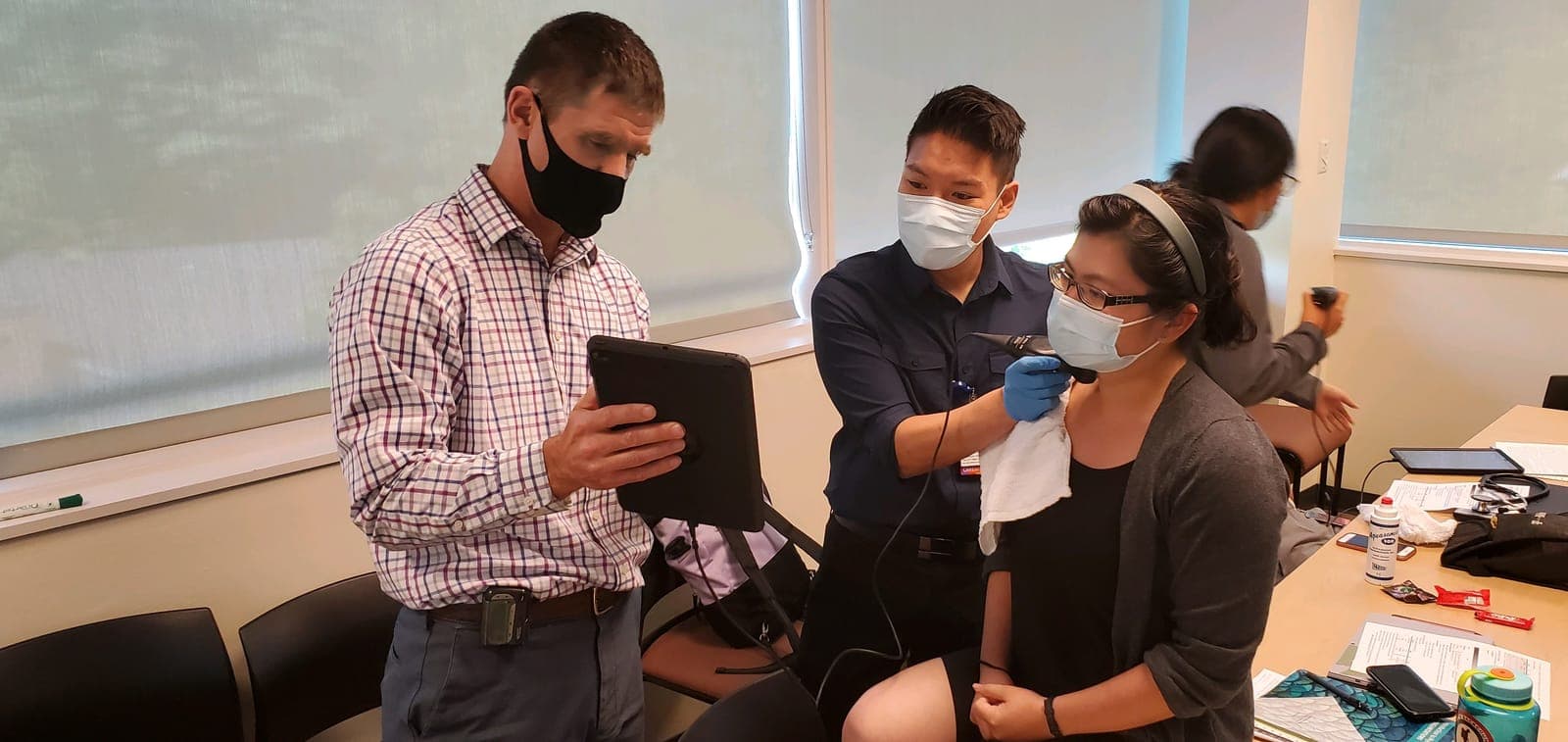 A faculty member reviewing ultrasound images on a tablet while residents scan a volunteer's neck