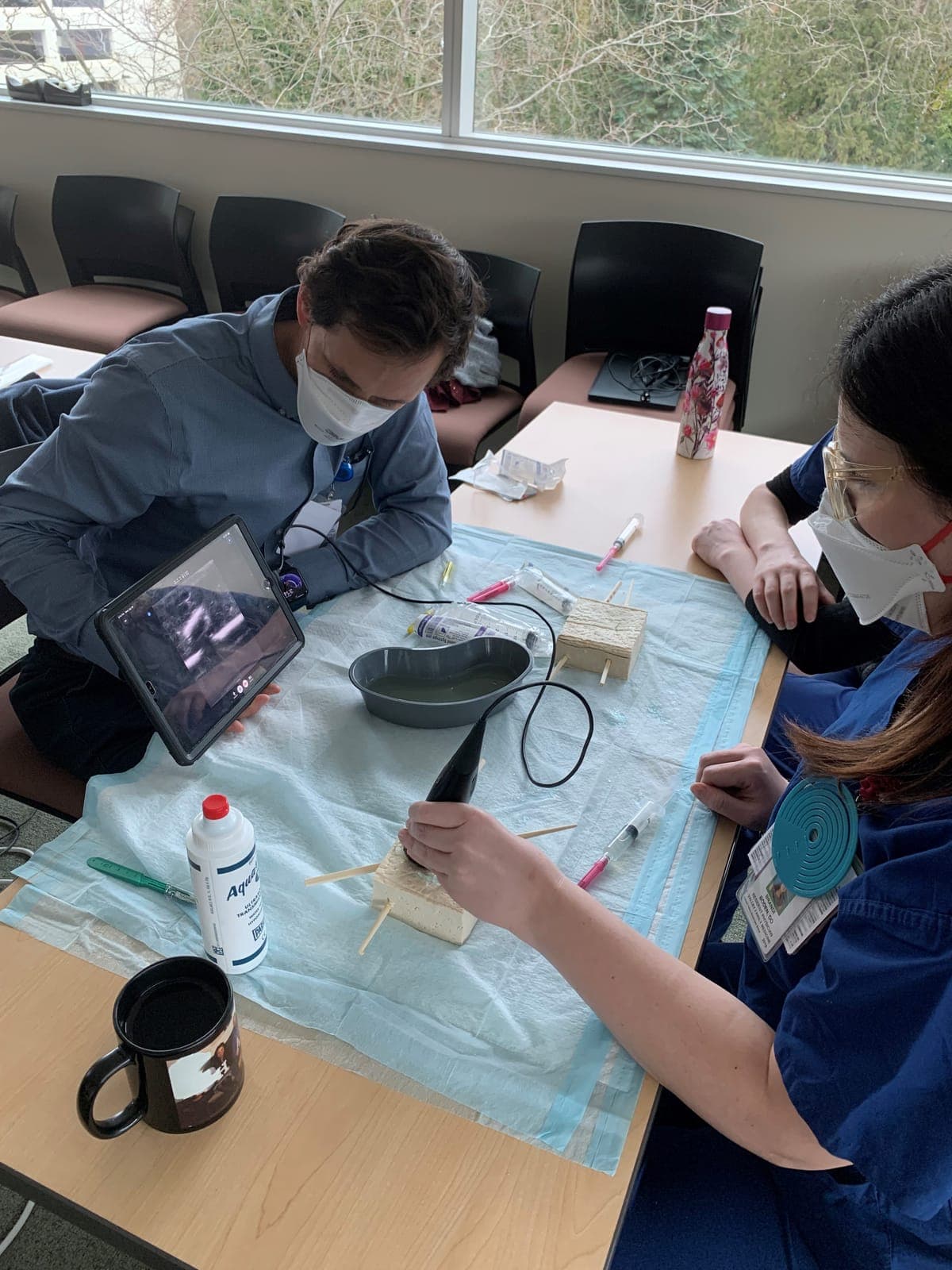 Residents practicing an ultrasound-guided needle procedure on a gel model while watching the image on a tablet