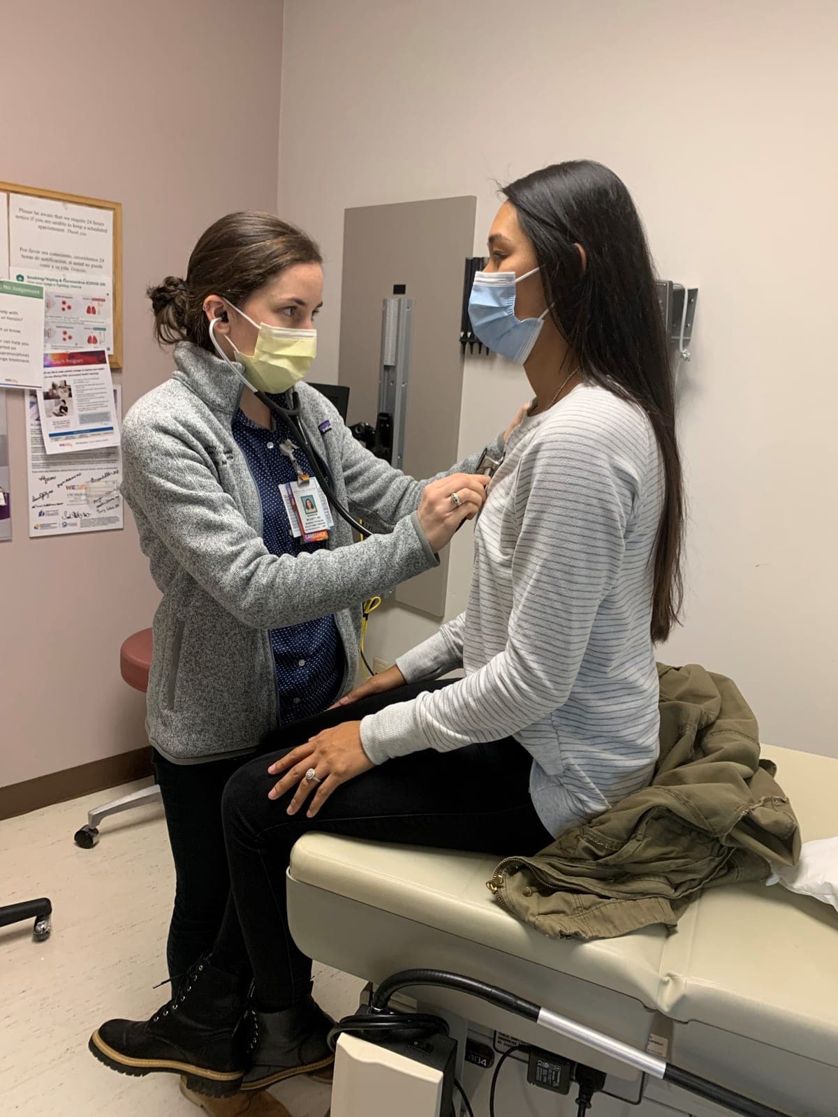 A resident listening with a stethoscope to a patient seated on an exam table in the clinic