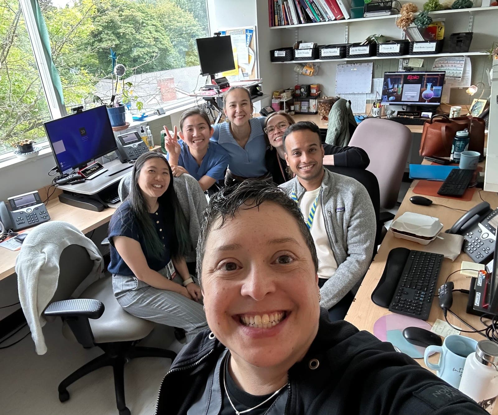 Six residents and faculty smiling together in a group selfie in the clinic workroom