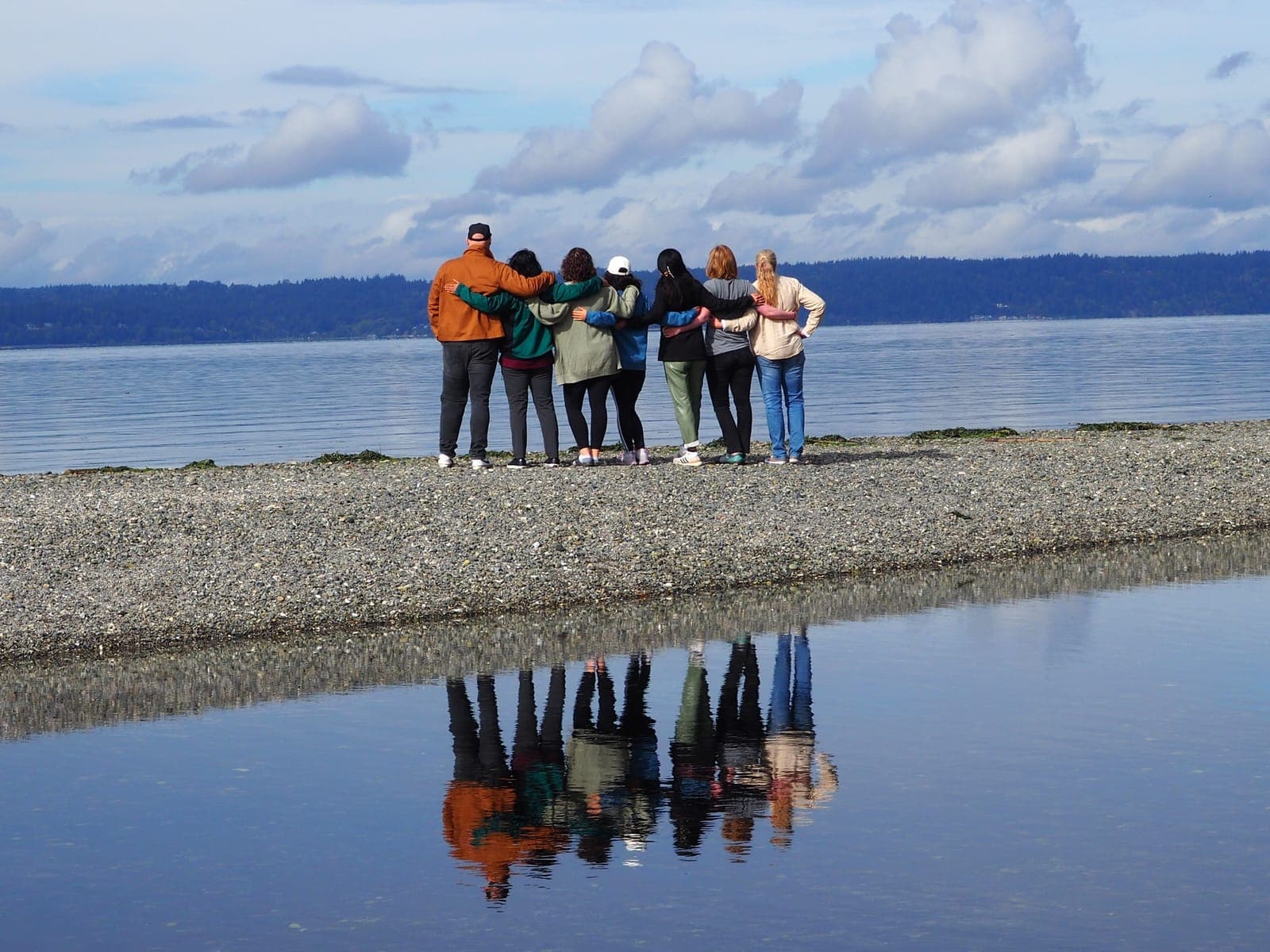 Residents seen from behind, arm in arm on a gravel spit looking out over Puget Sound