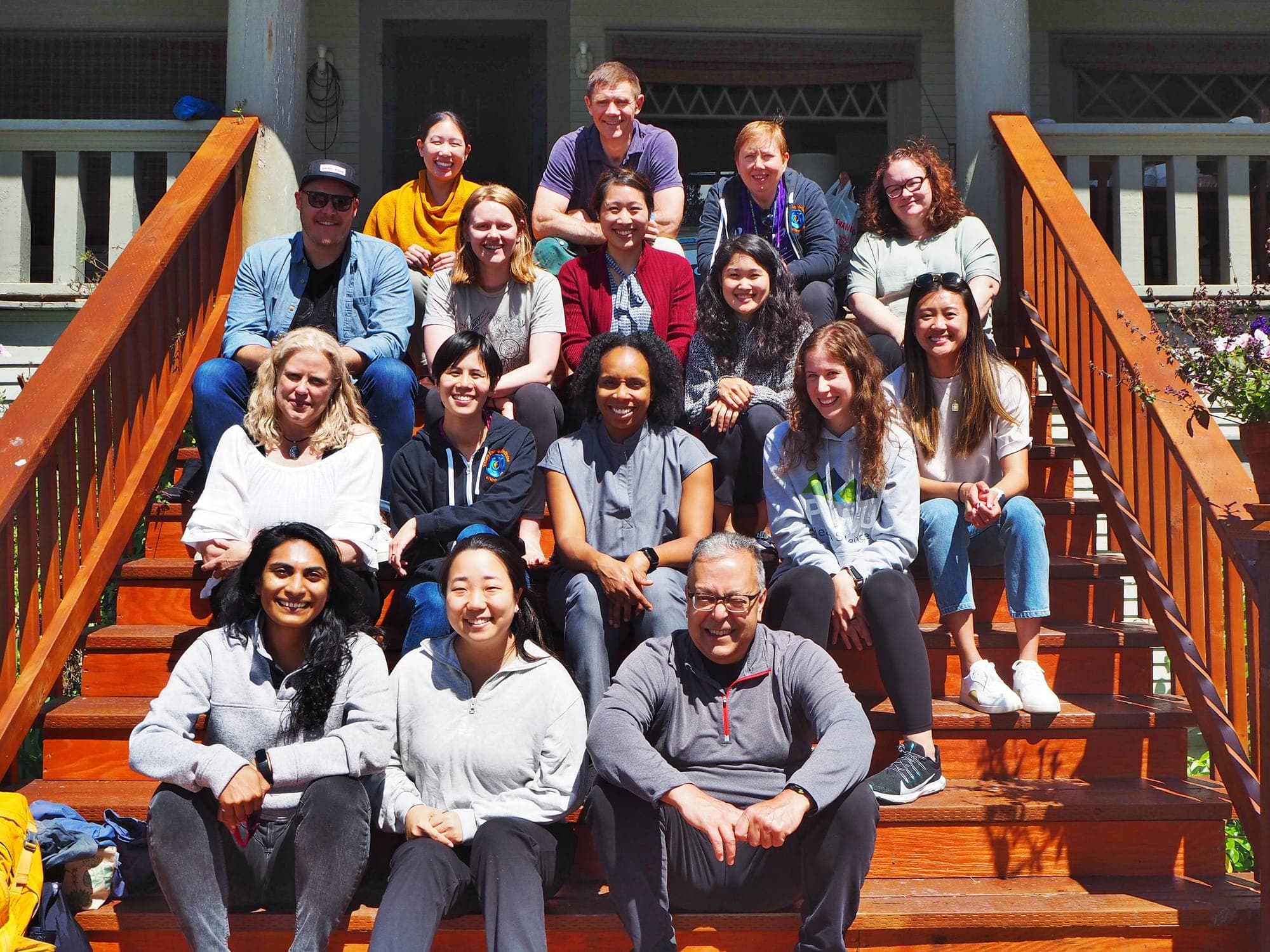 Residents and faculty sitting on the wooden front steps of a house at the class of 2025 intern retreat