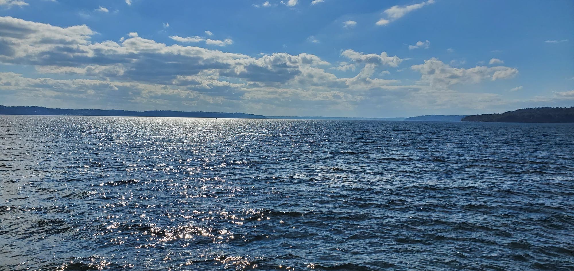 Sunlight on the open water of Puget Sound under scattered clouds
