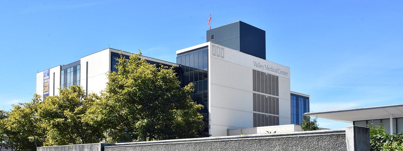 The Valley Medical Center hospital tower in Renton under a clear blue sky, with trees in front